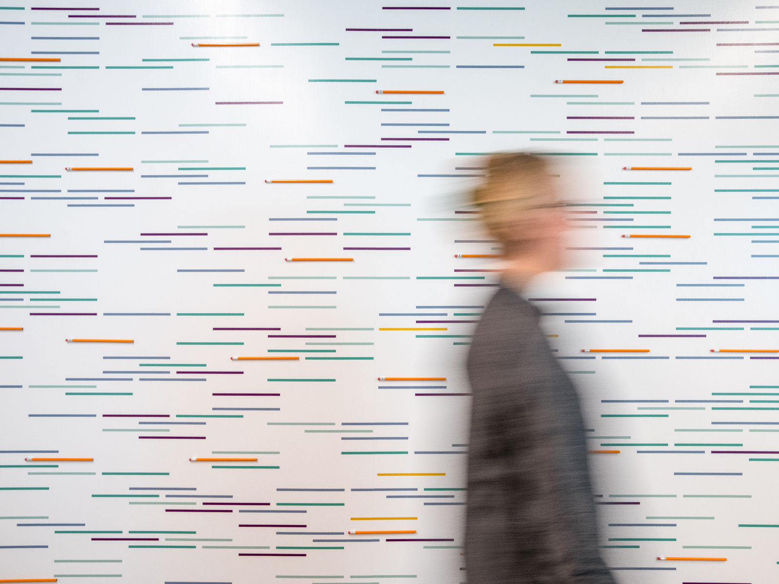 Person walking past a wall graphic that has colorful lines and pencils