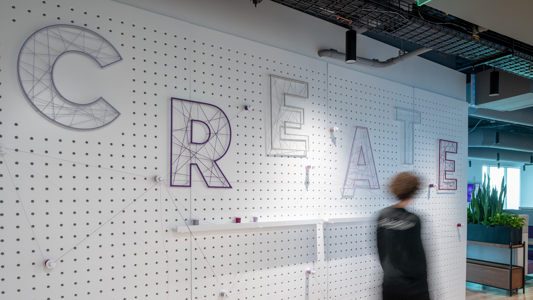 Person walking past peg board wall graphic with the word "CREATE"