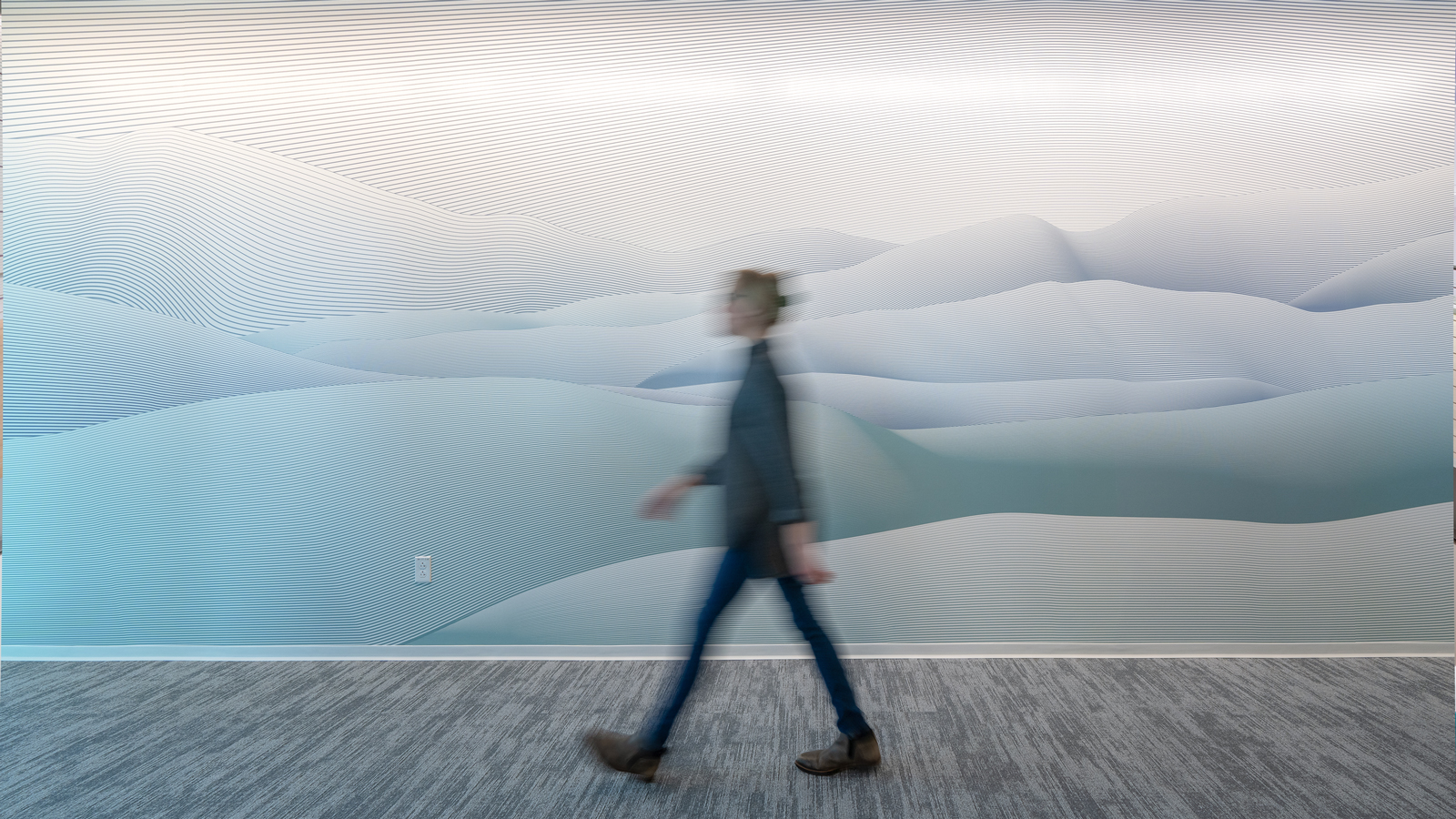 Person walking past wall graphic with linework mountain illustration