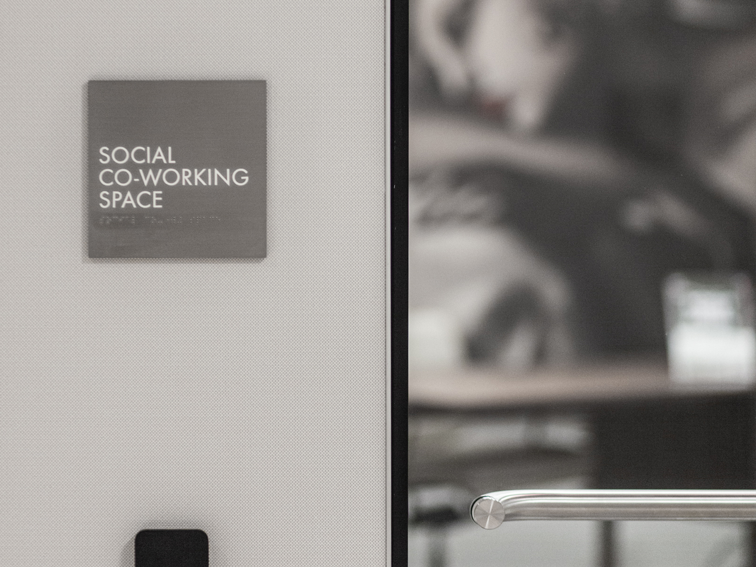 Detail shot ofmetal ADA sign, reads "SOCIAL CO-WORKING SPACE"