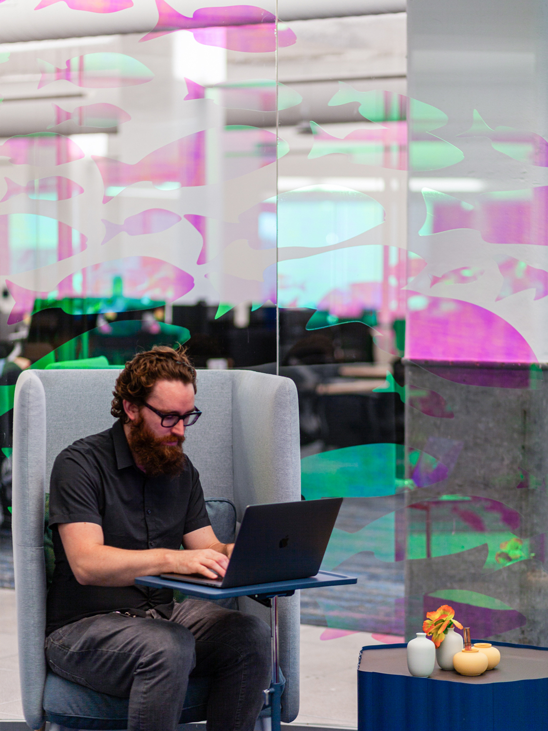 Dichroic graphics on glass depicting fish with a person in a chair using a laptop