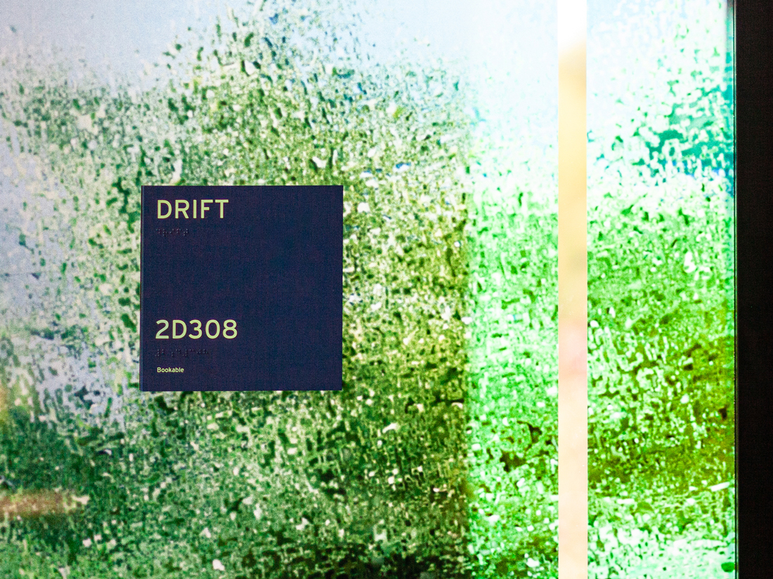 Detail image of textural green glass graphics with an ADA sign that reads "Drift"